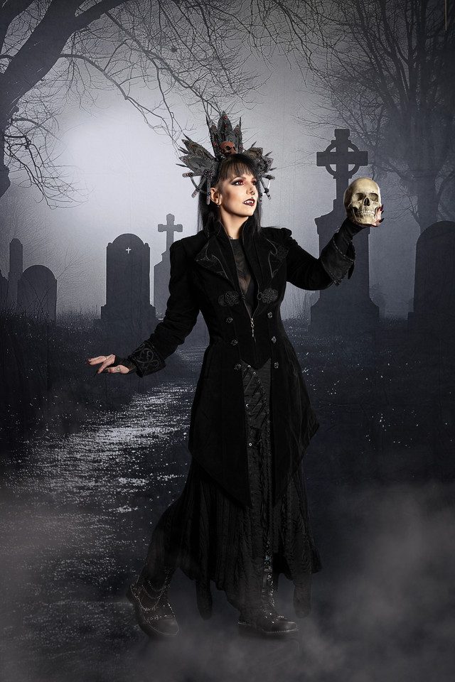 Person in gothic attire holding a skull in a foggy graveyard.
